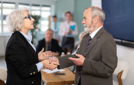 Senior male and female participants of meeting end business negotiations with handshake