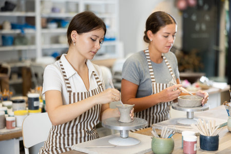 Two young women pottery workshop workers sculpt from raw clay