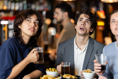 Group of emotional friends watch a sports match with interest in bar