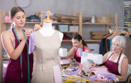 Mature head of manufacturing and female assistant sewing, young designer work with mannequin.