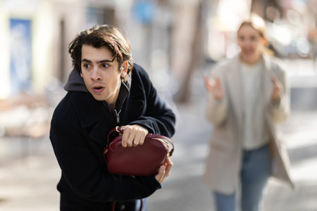 Young man snatching handbag from woman on street