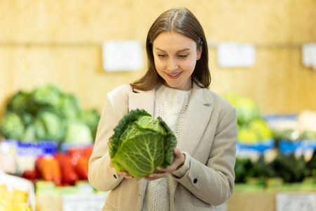 Female shopper selects cabbage at grocery store