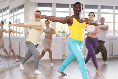 Positive African american man dancing and training movements Latin dance bachata during group class...