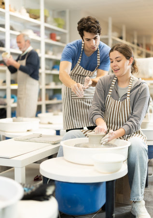 Young man helping young woman shape pottery on wheel