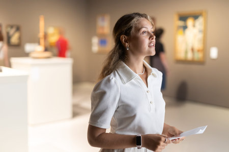 Woman with sheet piece of paper in hands view pictures and icons in museum hall