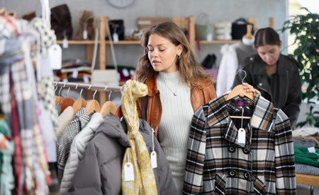 Uncertain young girl choosing winter coat in clothing store