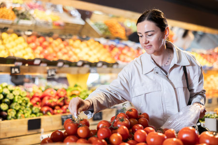 Middle-aged woman choosing tomatoes in grocery storeの写真素材