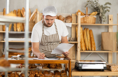 Bakery employee in apron examines documents, ponders debt restructuring