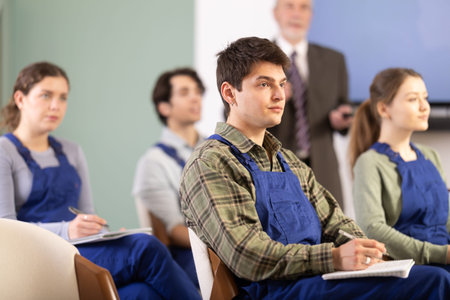 Young male student worker listening to lecture with teacher in background