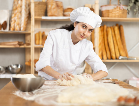 Young woman works in bakery as baker, kneads dough, works with flour.