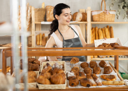 Young woman seller puts croissants in showcase
