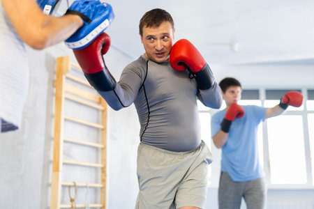 Man punching hits punch mitts is training with coach in box gymの写真素材
