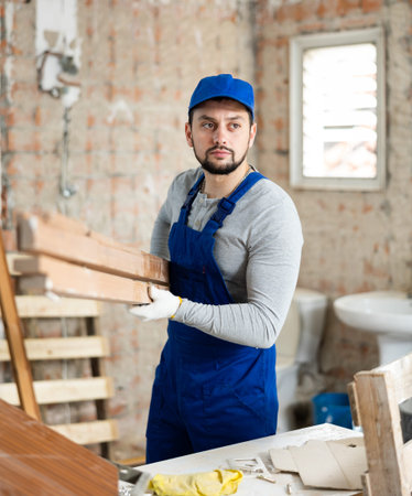 Worker in blue overalls carries planks to renovate roomの写真素材