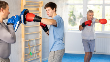 Guy in boxing gloves punching pads in hands of coach during workoutの写真素材