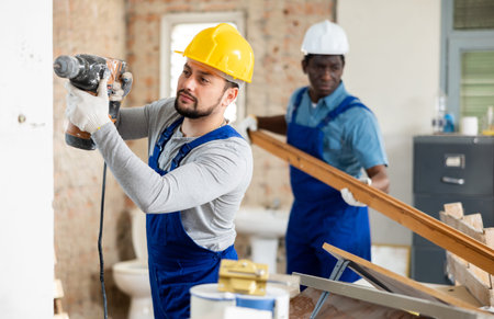 Room renovation - worker drills with puncher, another carries wooden planksの写真素材