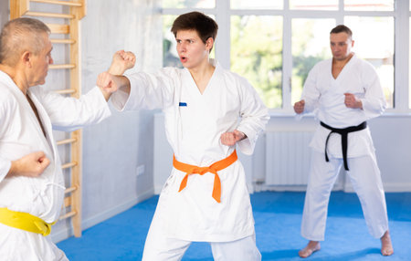 Guy honing punches during kumite with aged male opponent at karate trainingの写真素材