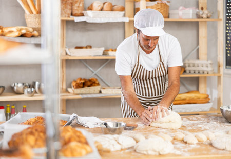Caucasian guy works in bakery as baker, kneads dough, works with flour.
