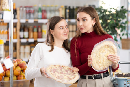 Teenage girl and her mother choosing pizza in grocery storeの写真素材