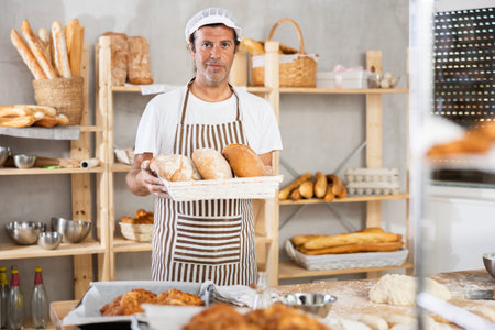 Portrait of baker holding tasty hot bread and baguettes in hands in kitchen
