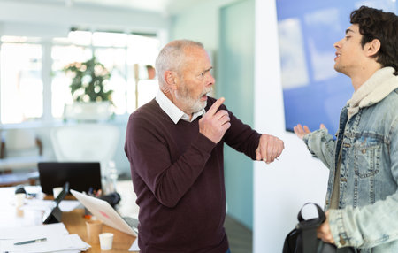 Elderly man scolding young male colleague for being late to office