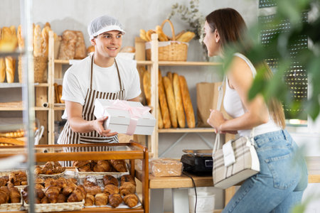Young bakery seller offering gift-wrapped box with baked treats to customer