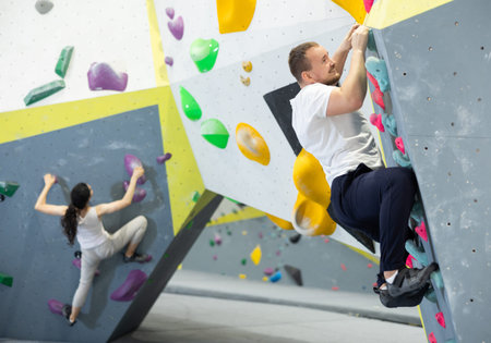 Man climbs steep artificial wall in sports complex and trains endurance and muscle strength. Active recreation in fitness center gym, types of recreation