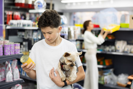 Teenage boy choosing canned dog food for Yorkshire terrier at pet store