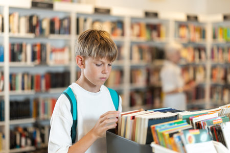 Teenage boy choosing books from display case table in bookstore
