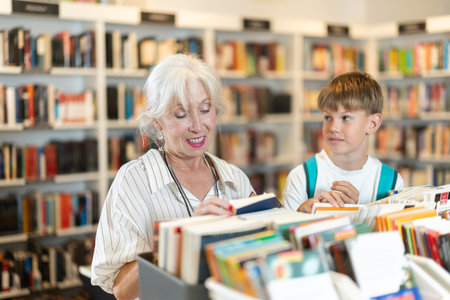 Happy grandmother with grandson choosing books from display case in bookstore
