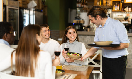 Man waiter serves cafe establishments couple visitor, puts food on table.