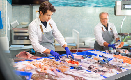 In fish shop, guy salesperson works at counter with seafood