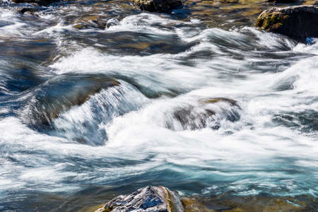 Creek or stream water flowing past rocks and stonesの写真素材