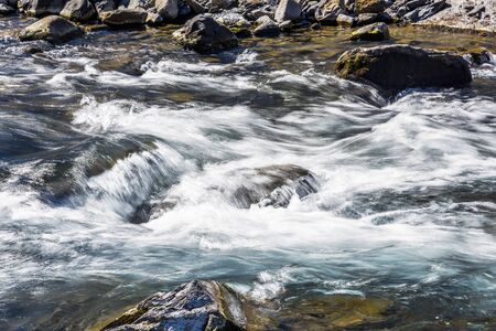 Creek or stream water flowing past rocks and stonesの写真素材