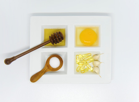 Set of healthcare beauty treatment, garlic capsule, honey and egg yoke on white ceramic plate and wooden spoons.の写真素材