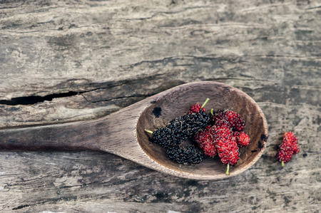 Mulberry red and black berry fruit in wooden spoon locates on a surface vintage wooden backgroundの写真素材