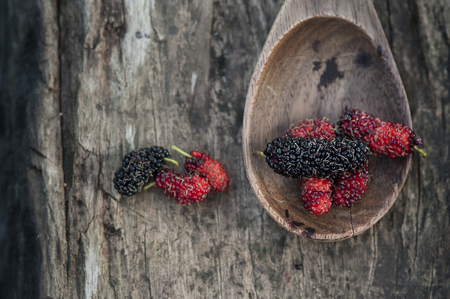 Mulberry red and black berry fruit in wooden spoon locates on a surface vintage wooden backgroundの写真素材