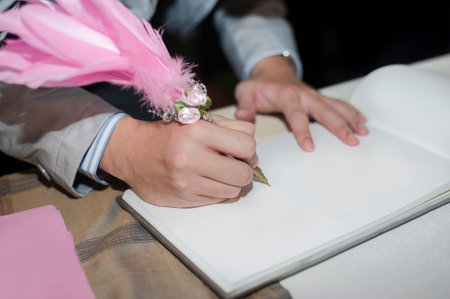 Men's hand signing guest book in wedding party with pen decorated with feather.の写真素材
