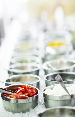 bowls of mixed fresh organic red peppers and vegetables in modern salad bar displayの写真素材