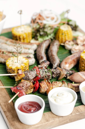 organic mixed grill barbecue meat platter rustic set meal with sausages, skewers, side dishes and sauces on white backgroundの写真素材
