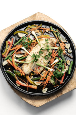 Chinese Cantonese style steamed spicy fish fillet with vegetables on a hot plateの写真素材