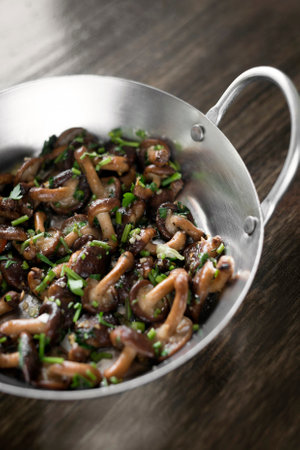 fried Shiitake mushrooms sauteed with garlic and herbs in metal pan on wood tableの写真素材