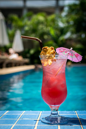 tropical singapore sling cocktail in tall glass by resort swimming pool