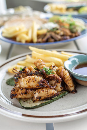 mediterranean style grilled squid with escabeche sauce and fries on white table at ibiza spain...