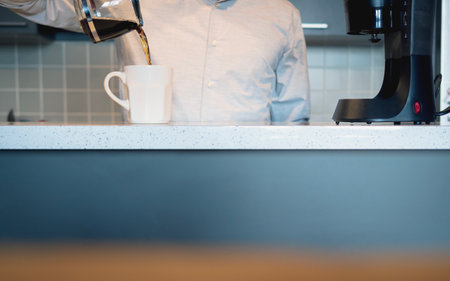 Man in the kitchen pouring a mug of hot filtered coffee from a glass pot in the morningの写真素材