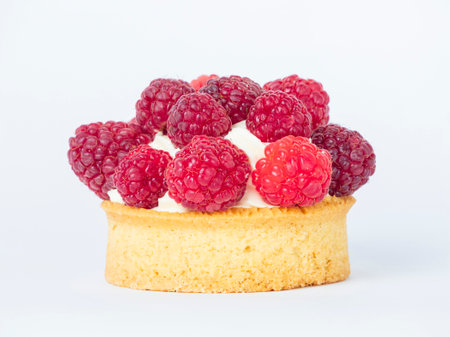 A small pastry with a raspberry filling sits on a white background. The pastry is topped with whipped cream and has a few raspberries on top. Concept of indulgence and luxuryの写真素材