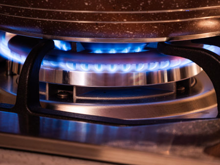 Blue flames burn brightly under a frying pan as it heats on a gas stove in a kitchen setting.