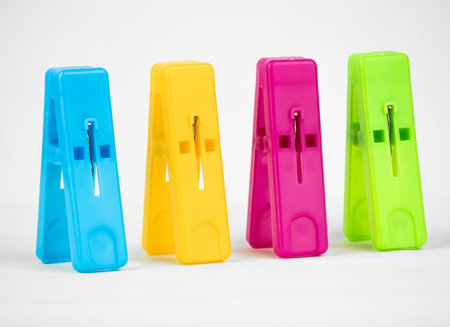 A collection of four colorful clothespins arranged neatly, showcasing vibrant blue, yellow, pink, and green shades against a clean white backgroundの写真素材