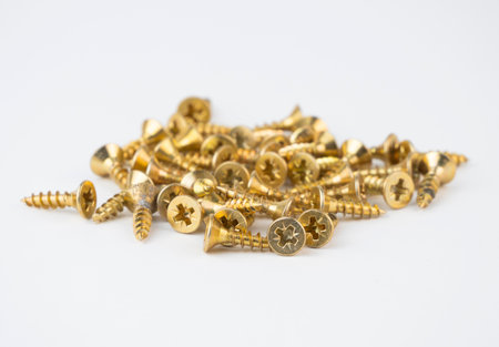 A pile of golden screws lies on a white surface ready for various projectsの写真素材