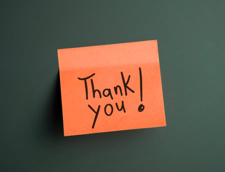 Bright orange sticky note with a handwritten thank you message on a dark backgroundの写真素材