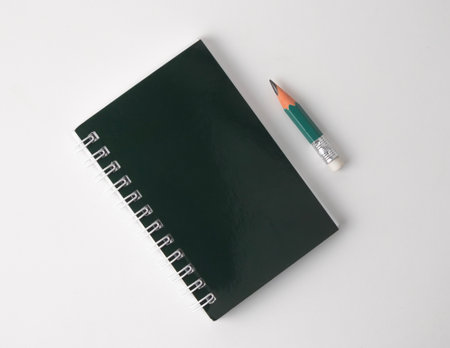 A spiral notebook sits next to a pencil on a white backgroundの写真素材